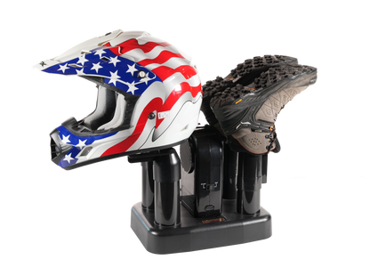 A black helmet and shoe dryer holding a black athletic shoe, with a white motocross helmet featuring a red, white, and blue American flag star pattern resting on the left side, isolated on a white background.